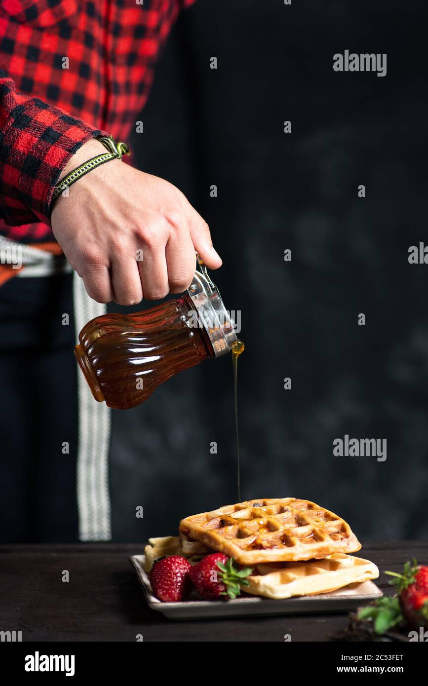 Homme ajoutant du miel sur un dessert de gaufres fraîches Banque D'Images