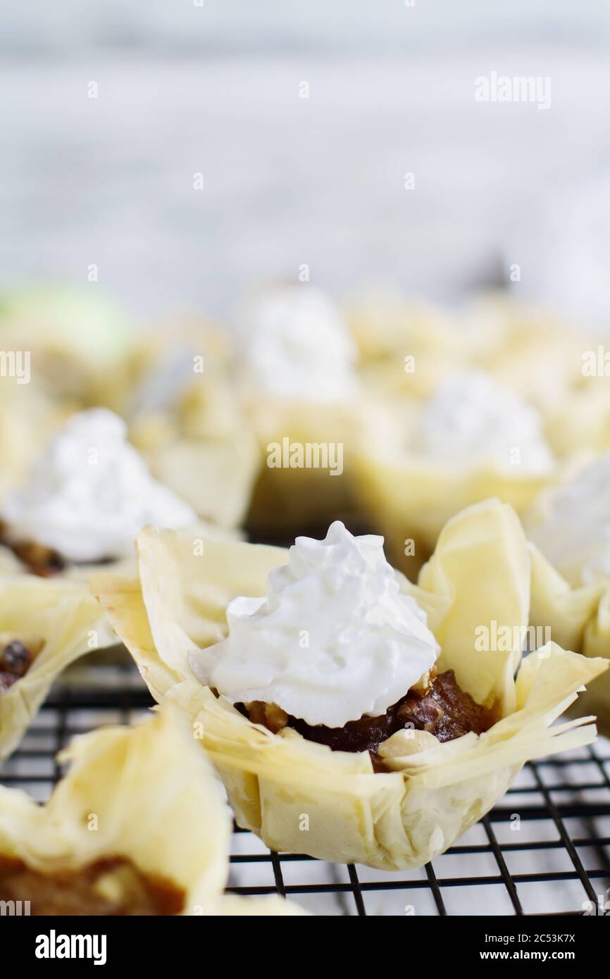 Mini-chaussons aux pommes avec croûte phyllo et crème fouettée sur un support de boulangers. Mise au point sélective avec arrière-plan flou. Banque D'Images