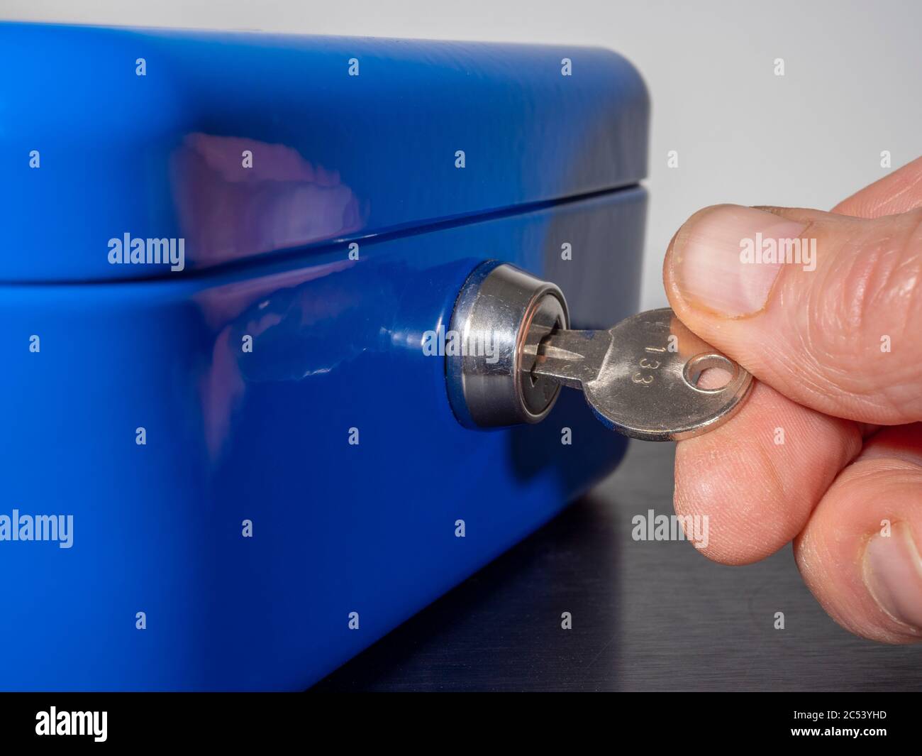 Les doigts d'un homme tournant la clé numérotée dans la serrure d'un coffre-fort/coffre-fort en métal peint en bleu. Banque D'Images