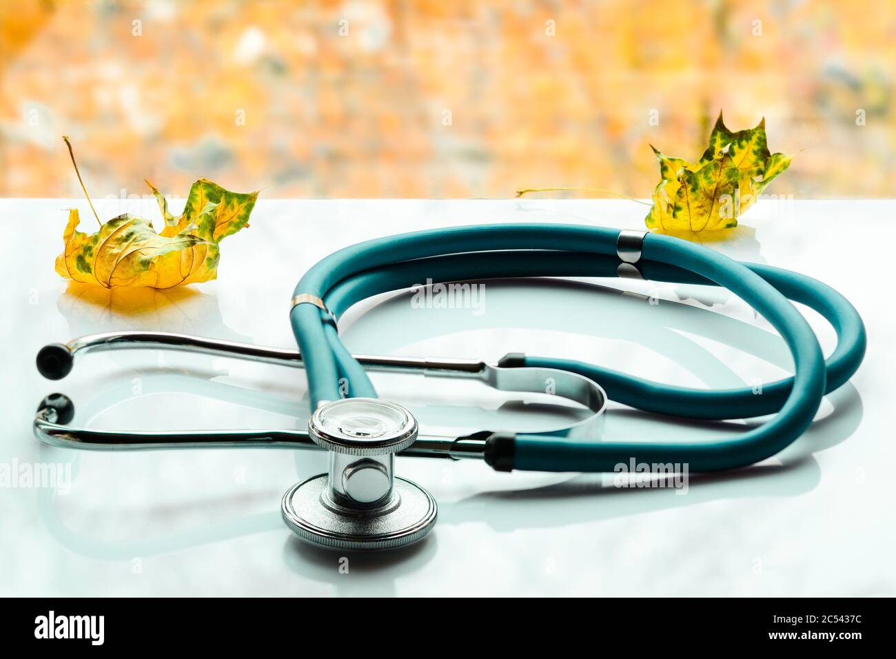 Stéthoscope et feuilles jaunes sur une table blanche du médecin, avec des couleurs automnales à l'extérieur de la fenêtre. Concept de traitement de la saison du rhume et de la grippe. Banque D'Images