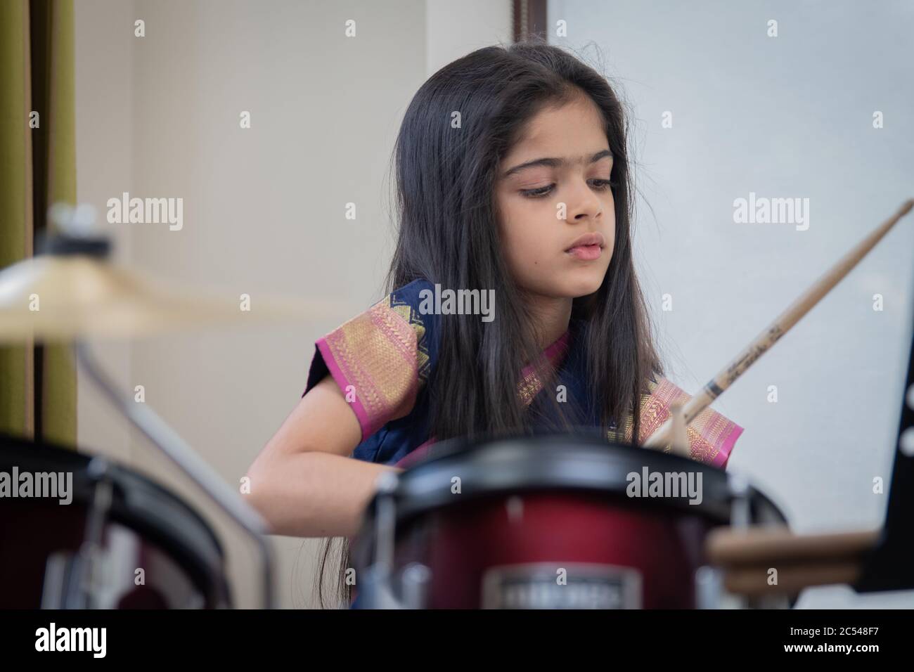 Âge scolaire fille indienne britannique jouant la batterie dans une saree. Banque D'Images