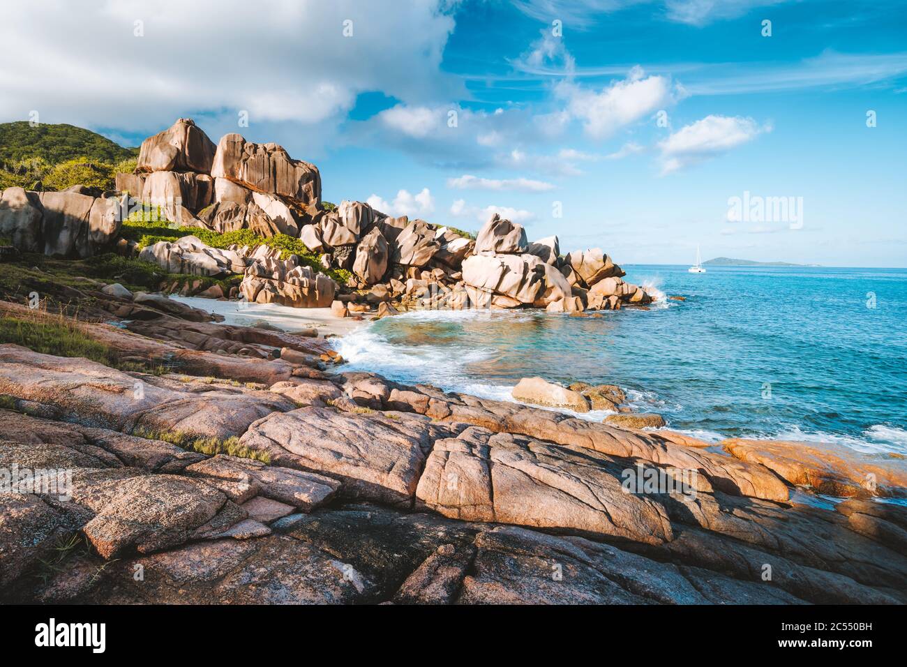 Plage Éloignée Grand L Anse, La Digue, Seychelles. Côte tropicale de l'océan, rochers de granit uniques et bateau à voile solitaire en mer. Banque D'Images
