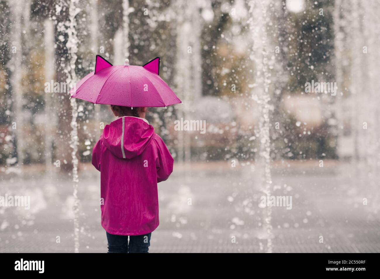 Enfant fille de 4-5 ans portant un imperméable tenant un parapluie sur un arrière-plan de pluie gros plan. Vue arrière. Saison d'automne. Banque D'Images