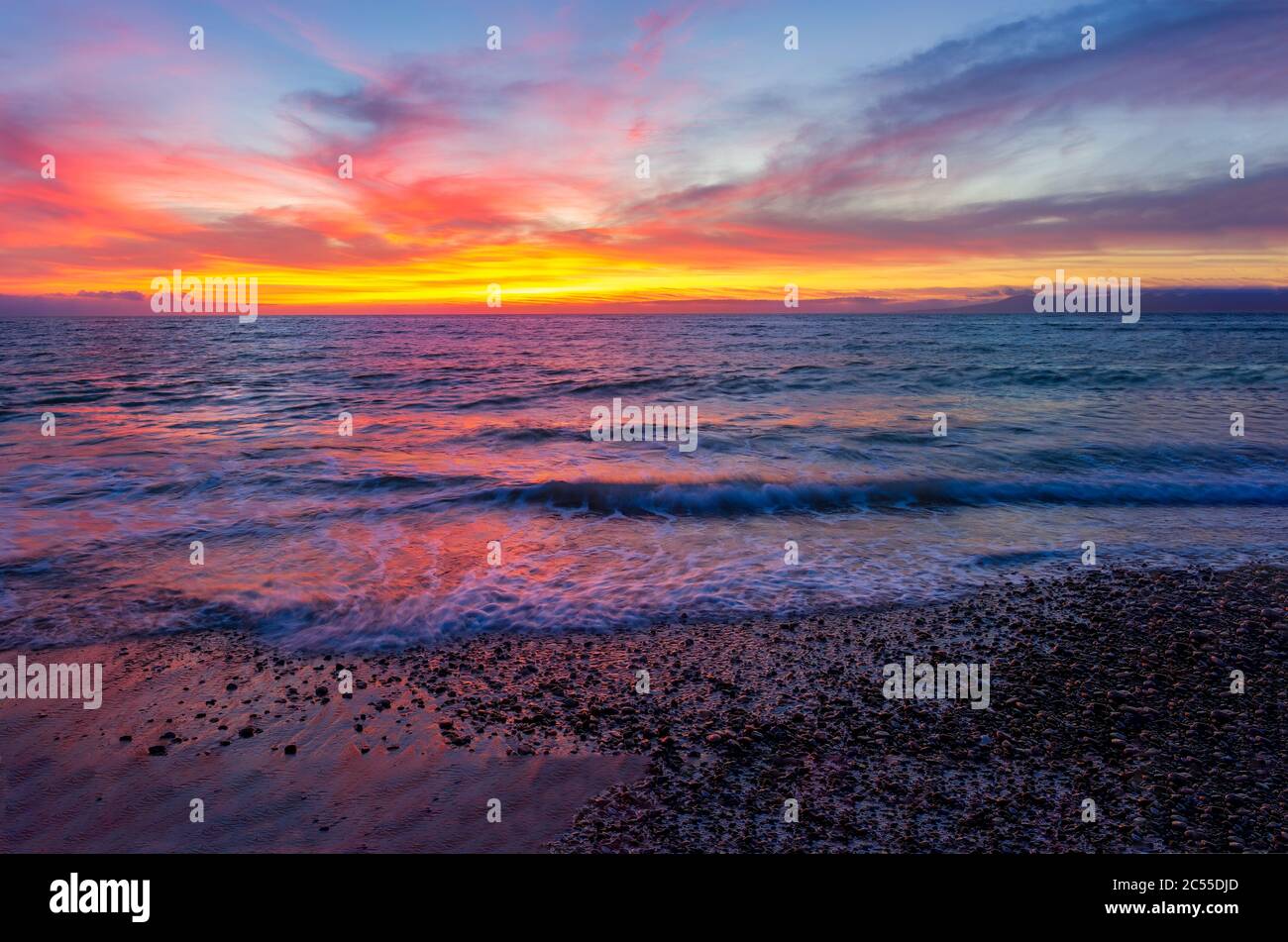 Un ciel coloré de coucher de soleil sur l'océan comme une vague douce roule à terre Banque D'Images