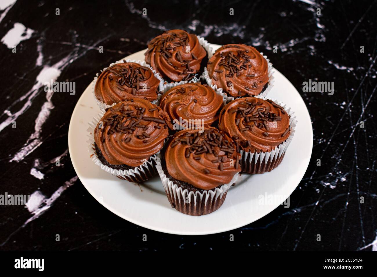 Cupcakes au chocolat centrés sur une assiette blanche sur un fond noir marbré avec espace de copie Banque D'Images