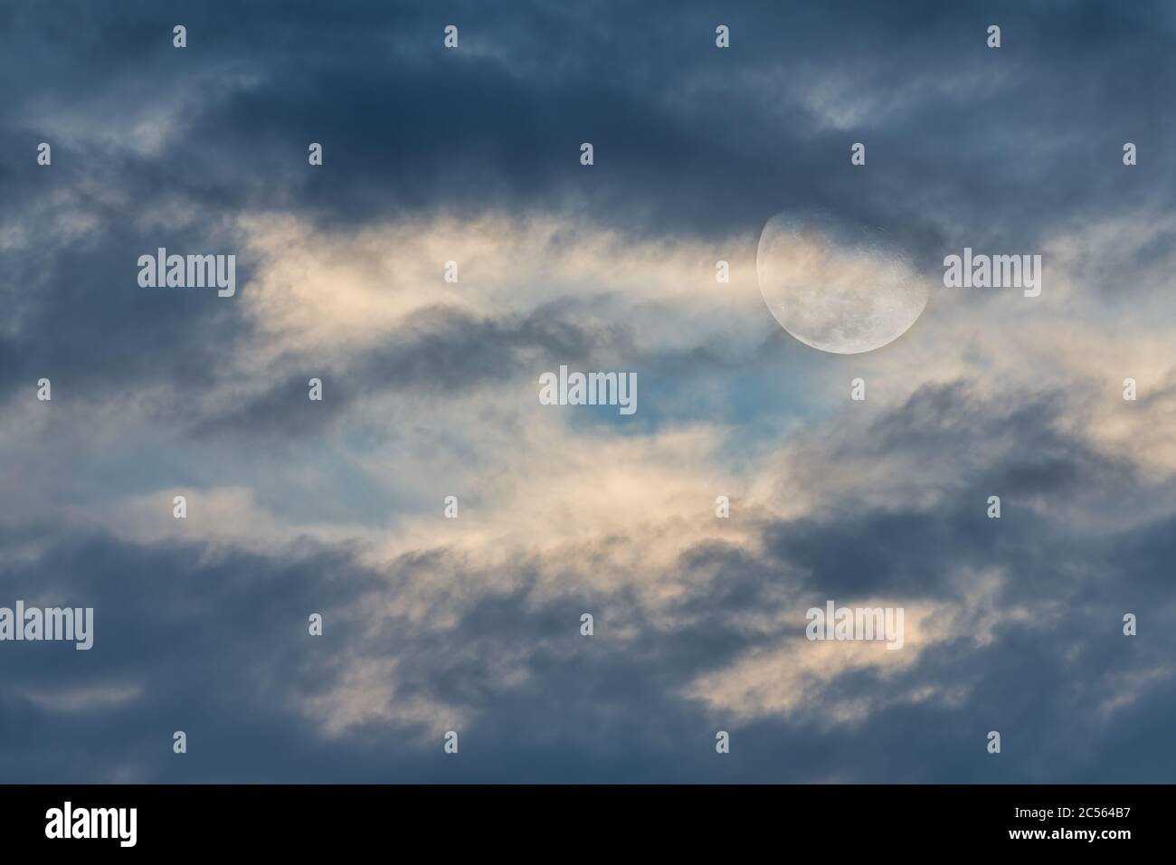 Une pleine lune se lève parmi les nuages dans un ciel de jour Banque D'Images