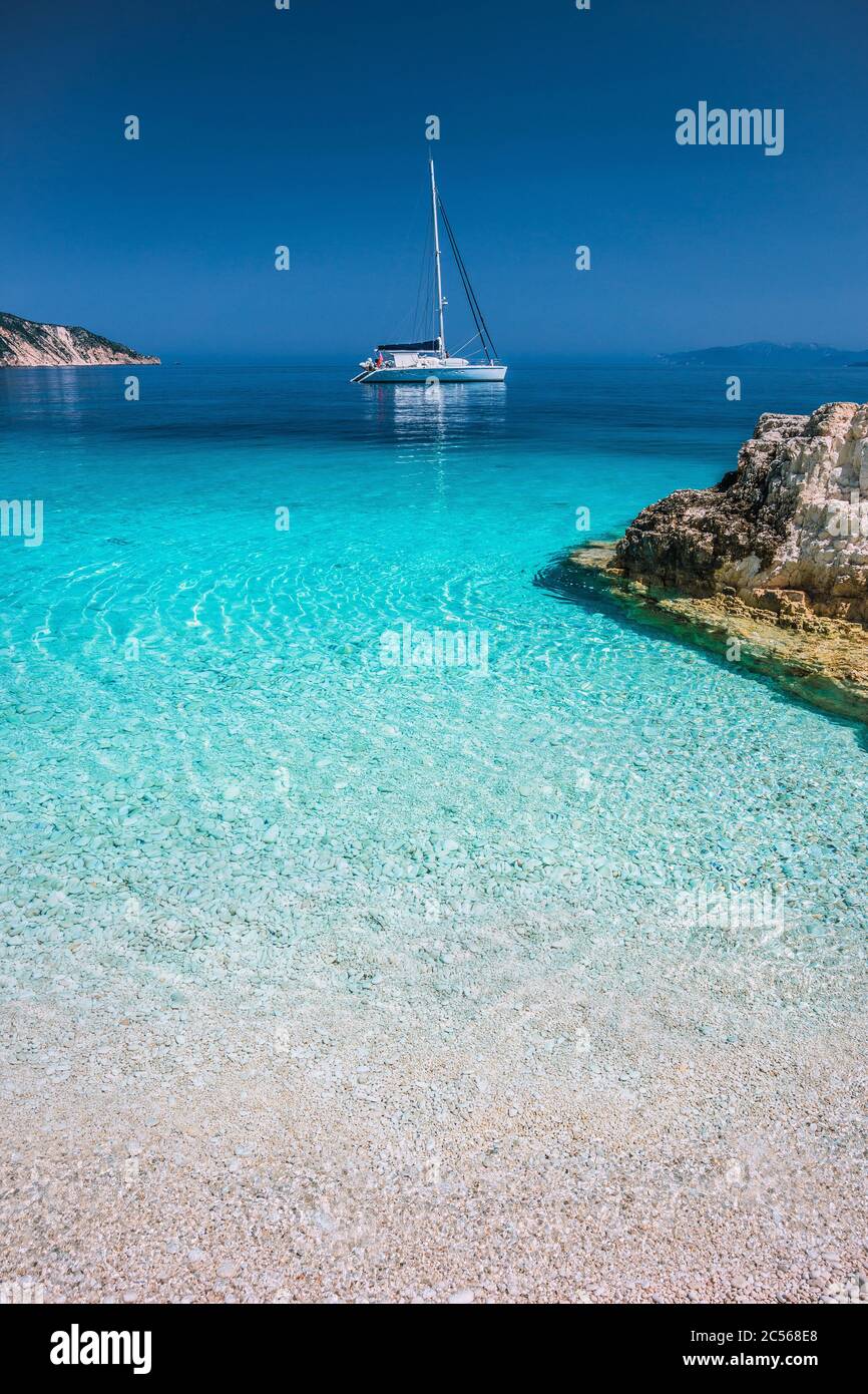Vacances. Lagon bleu Azur avec vagues tranquilles et bateau à voile en catamaran avec littoral en arrière-plan. Banque D'Images