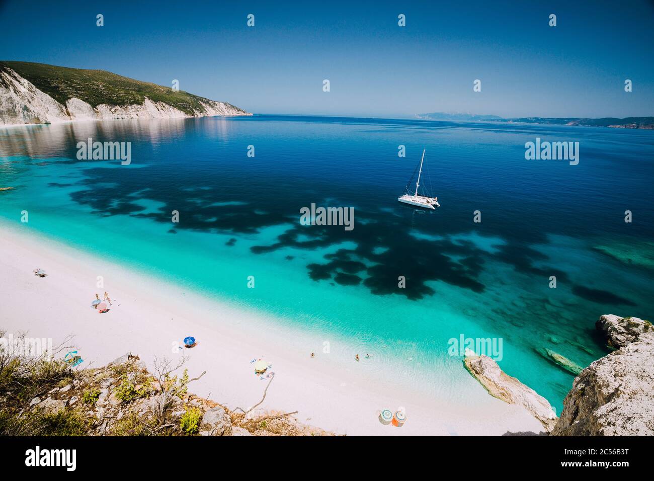 Catamaran blanc dans l'eau de mer bleu clair. Touristes sur la plage de sable près de la lagune de mer d'Azure. Kefalonia, Grèce. Banque D'Images