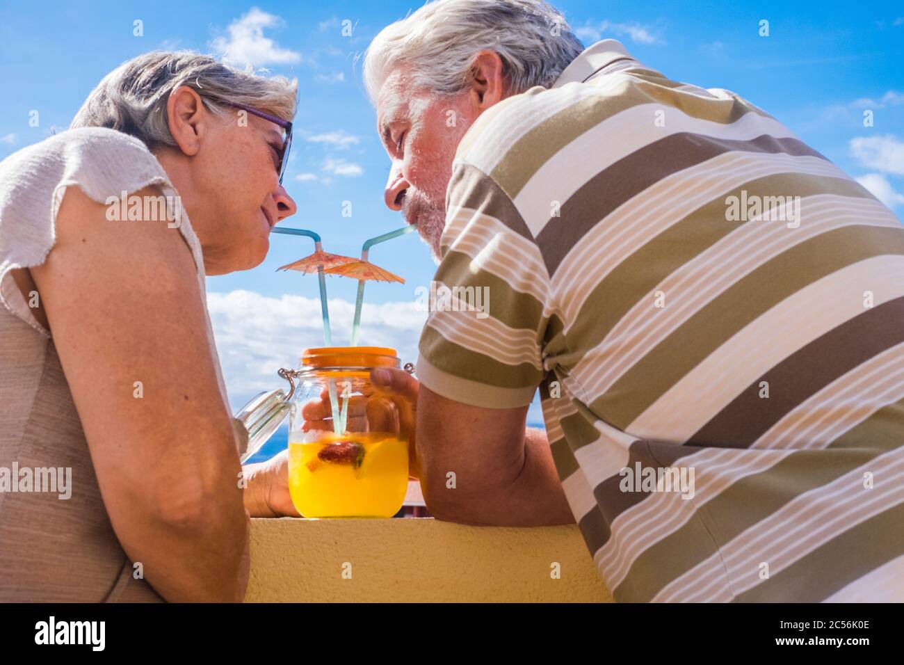 L'homme et la femme adulte âgé de 60 ans de boire des jus de fruits sains d'une piscine en verre vase la terrasse. Belle vue et de belles personnes. Banque D'Images