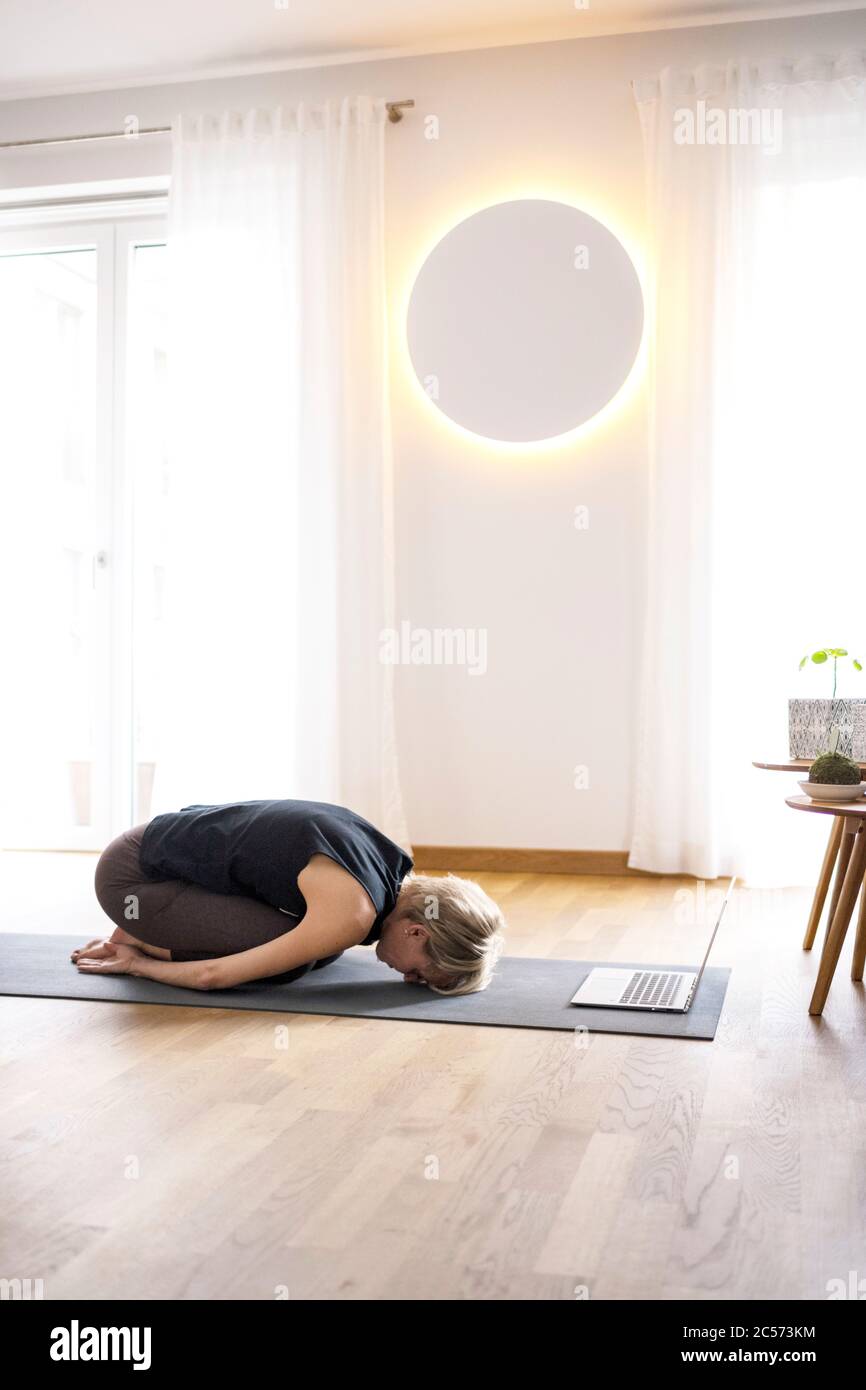 Femme 40+ pratique le yoga à la maison avec un ordinateur portable. Cours de yoga en ligne. Banque D'Images