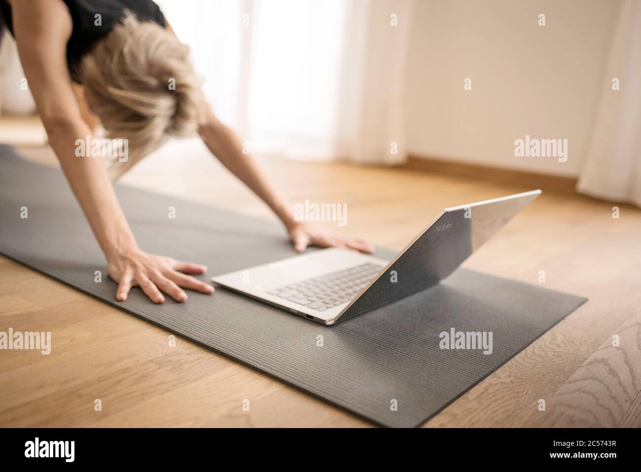 Femme 40+ pratique le yoga à la maison avec un ordinateur portable. Cours de yoga en ligne. Banque D'Images