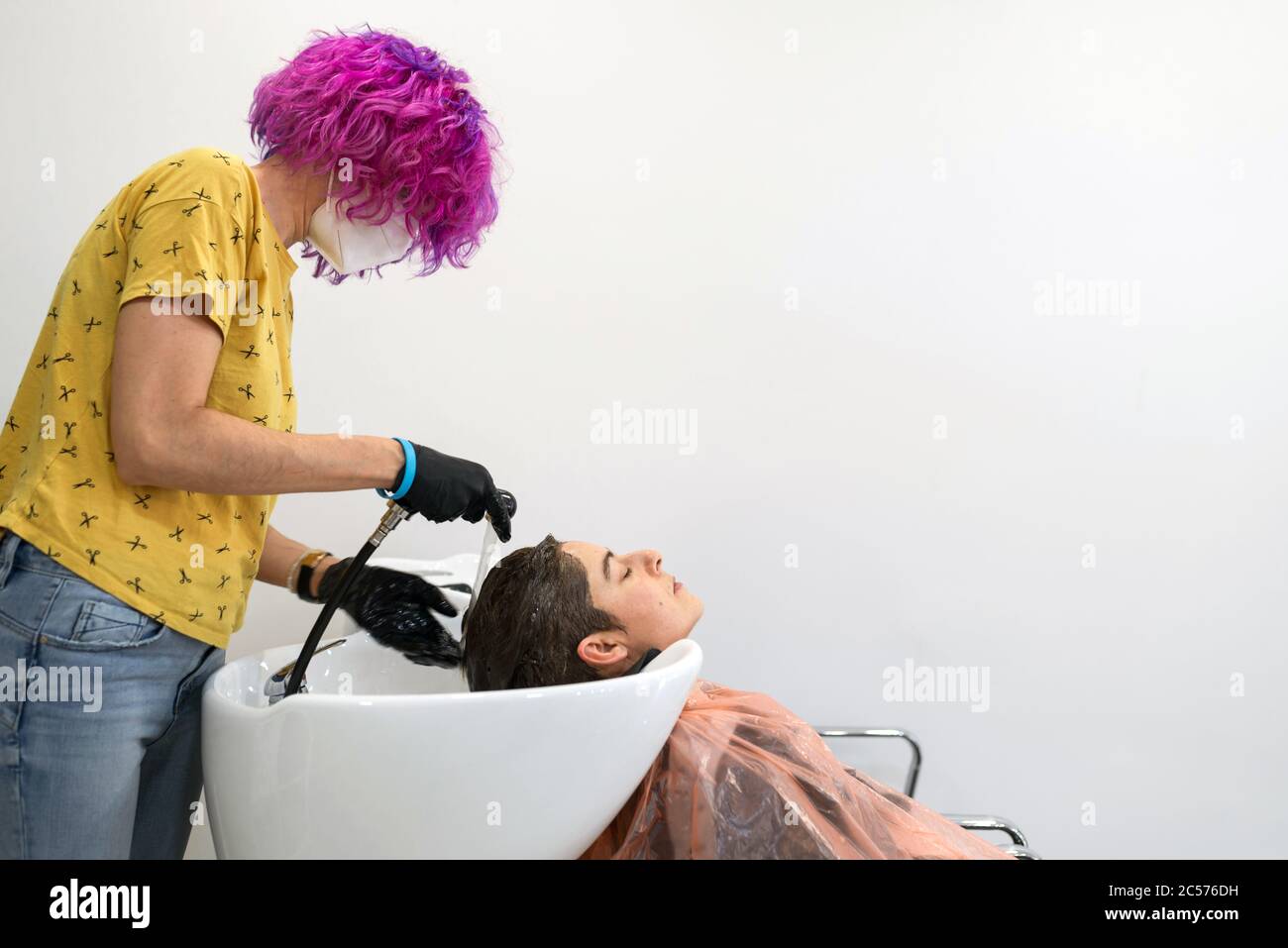 Concept: Unconfinement après le coronavirus, Covid-19. Coiffeur professionnel avec cheveux violets. Laver la tête d'une femme après avoir coupé ses cheveux, teindre Banque D'Images