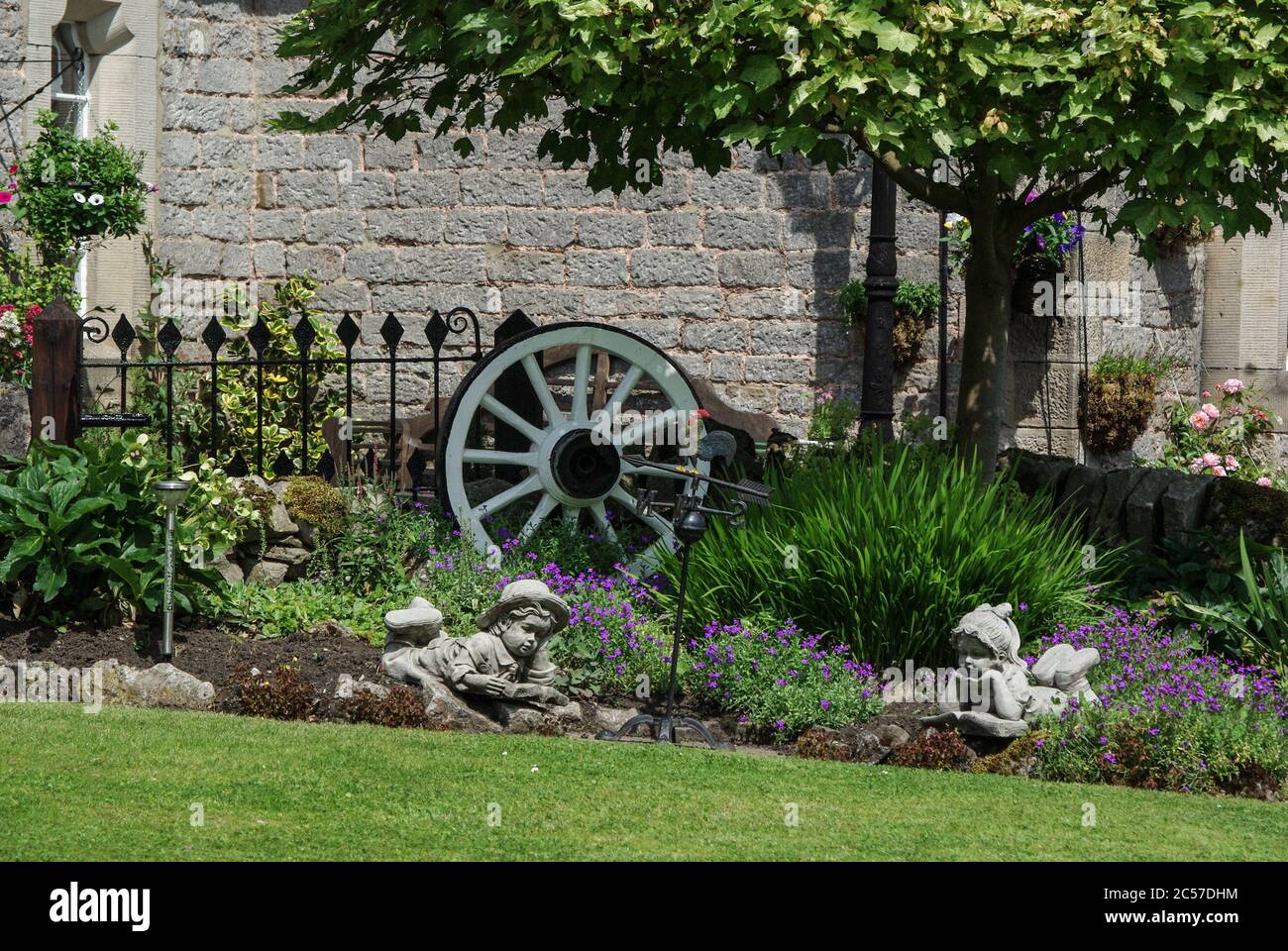 Jolie bordure de jardin, avec des figures de pierre inclinable et une roue de chariot bleue, dans le village de domaine d'Ilam, Staffordshire, Royaume-Uni Banque D'Images