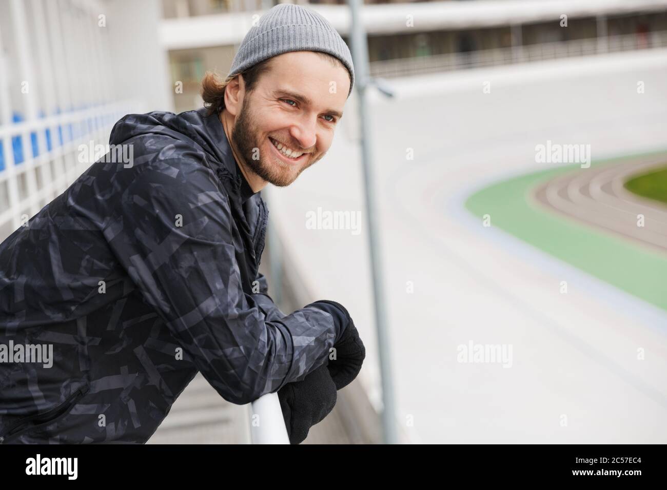 Jeune sportif attrayant et souriant, se reposant après l'entraînement au stade, sur un rail Banque D'Images