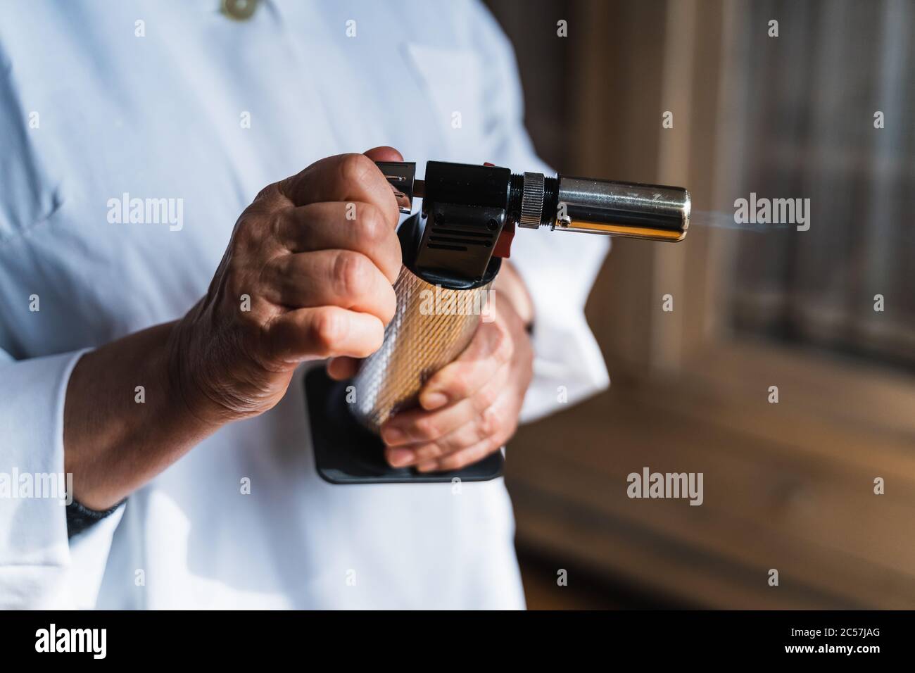 Détail des mains d'un cuisinier à l'aide d'une lampe de cuisine avec la flamme qui s'échappe Banque D'Images