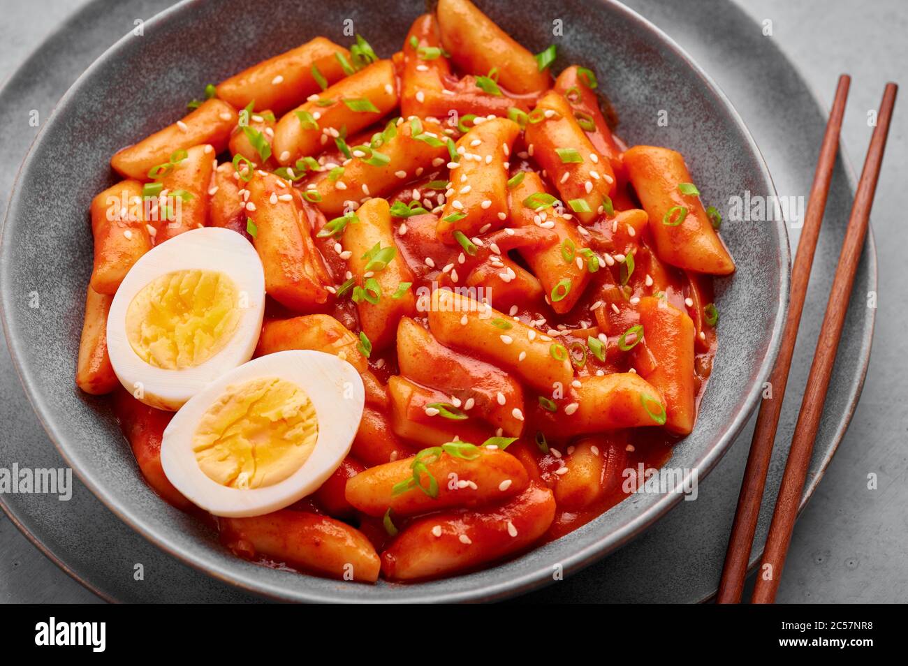 Tteokbokki avec œufs dans un bol gris sur une table en béton. Le tteok-bokki est un plat de cuisine coréenne composé de gâteaux de riz. Cuisine asiatique. Banque D'Images