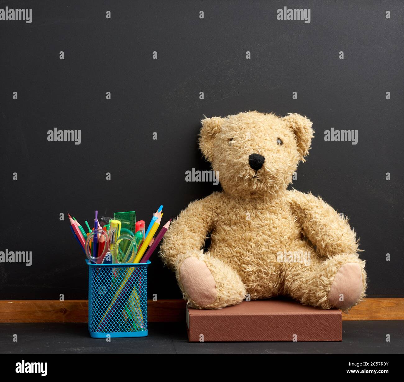 papeterie et ours en peluche marron assis sur le fond d'un tableau noir vide de craie, concept de retour à l'école Banque D'Images