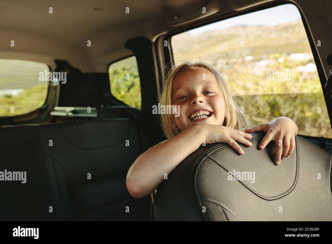 Belle fille assise sur le siège arrière de la voiture. Fille souriante voyageant en voiture. Banque D'Images