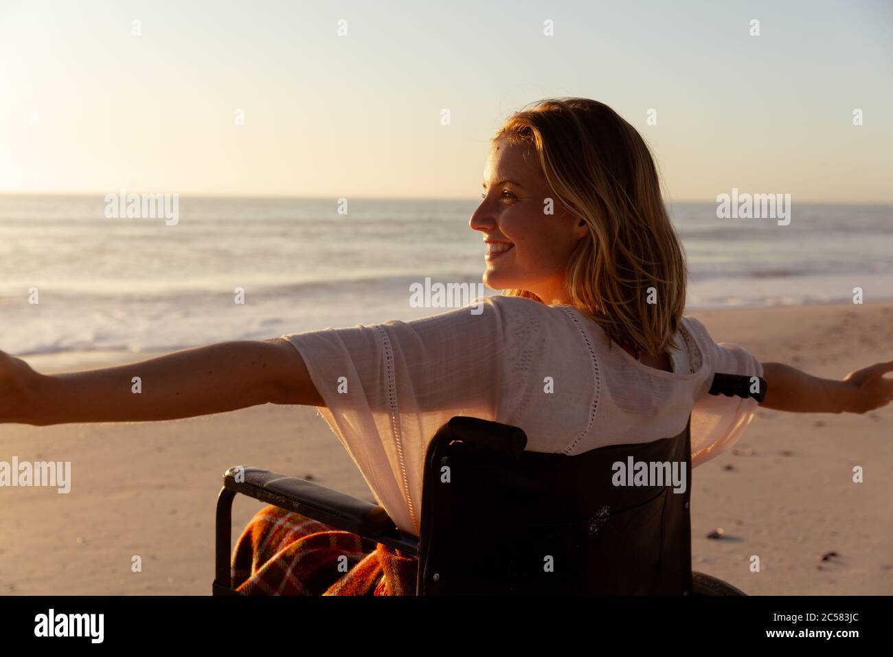 Femme souriante en fauteuil roulant avec ses bras ouverts à la plage Banque D'Images
