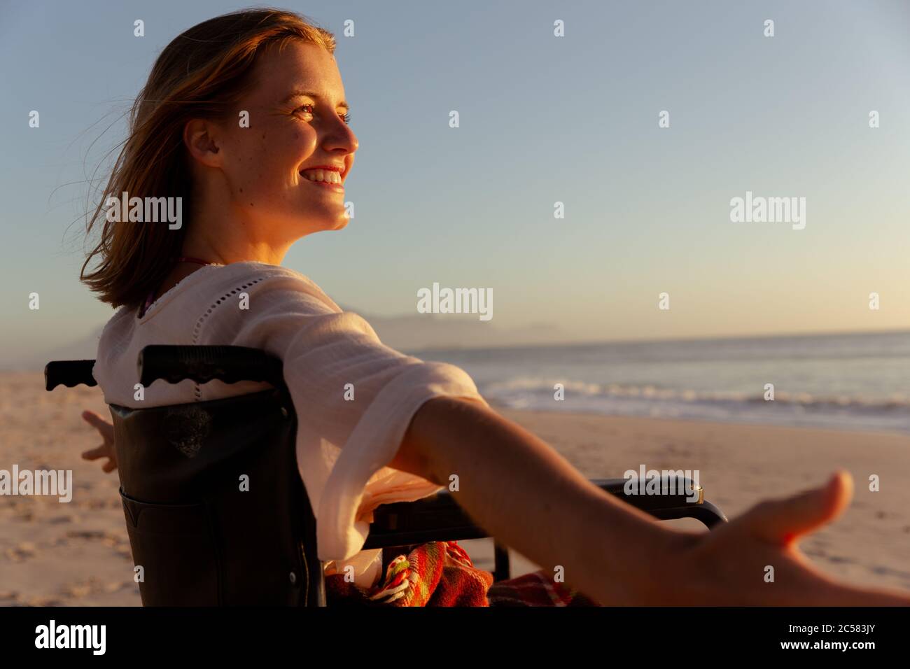 Femme souriante en fauteuil roulant avec ses bras ouverts à la plage Banque D'Images