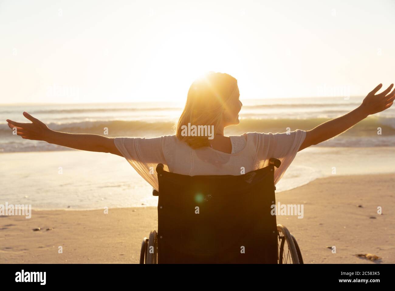Vue arrière d'une femme en fauteuil roulant avec ses bras larges ouverts à la plage Banque D'Images