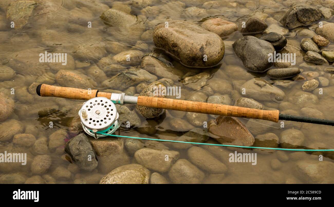 Pêche à la mouche à la mouche, pêche à la canne à saumon et à la bobine reposant sur des rochers humides au bord d'une rivière. Banque D'Images