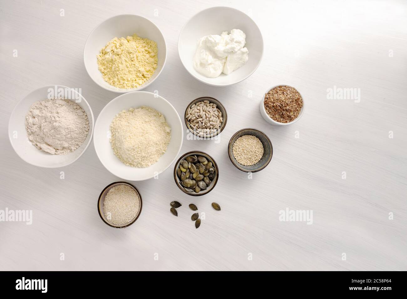 Ingrédients de cuisson pour un pain sain à faible teneur en glucides avec du fromage blanc, du son d'avoine, de la farine d'amande et de diverses graines sur une table blanche, vue en grand angle de l'ab Banque D'Images
