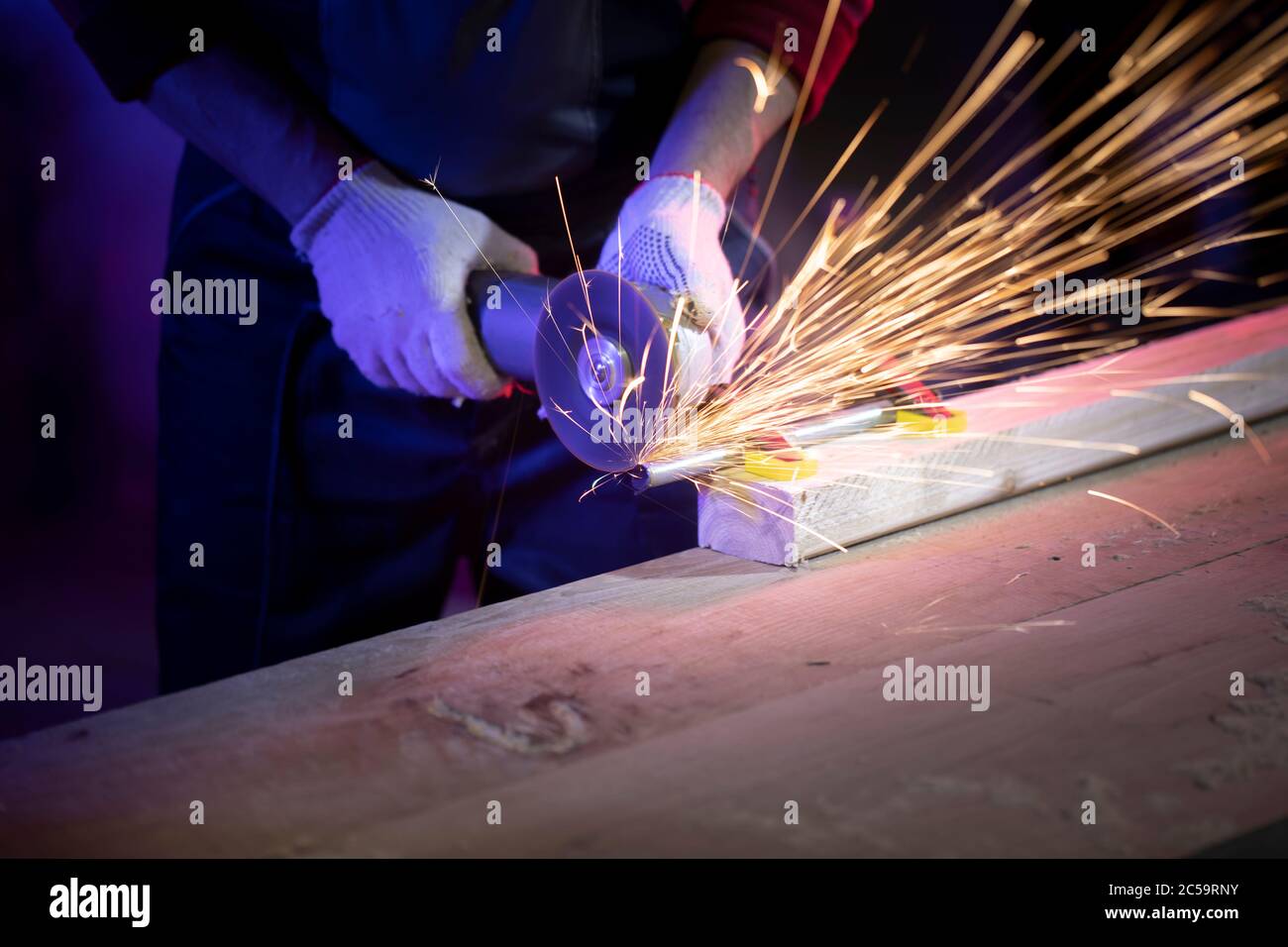 gros plan des mains d'hommes dans des gants meulant le métal avec des  étincelles dans la lumière colorée Photo Stock - Alamy