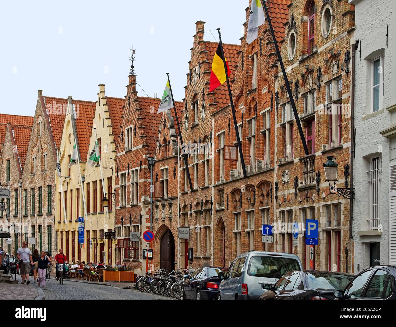 Scène de rue incurvée, pavés, vieux bâtiments, architecture flamande, toits de galets escarpés, vélos, voitures garées, personnes, drapeaux, Flandre, Bruges, E Banque D'Images Scène de rue incurvée, pavés, vieux bâtiments, architecture flamande, toits de galets escarpés, vélos, voitures garées, personnes, drapeaux, Flandre, Bruges, E Banque D'Images