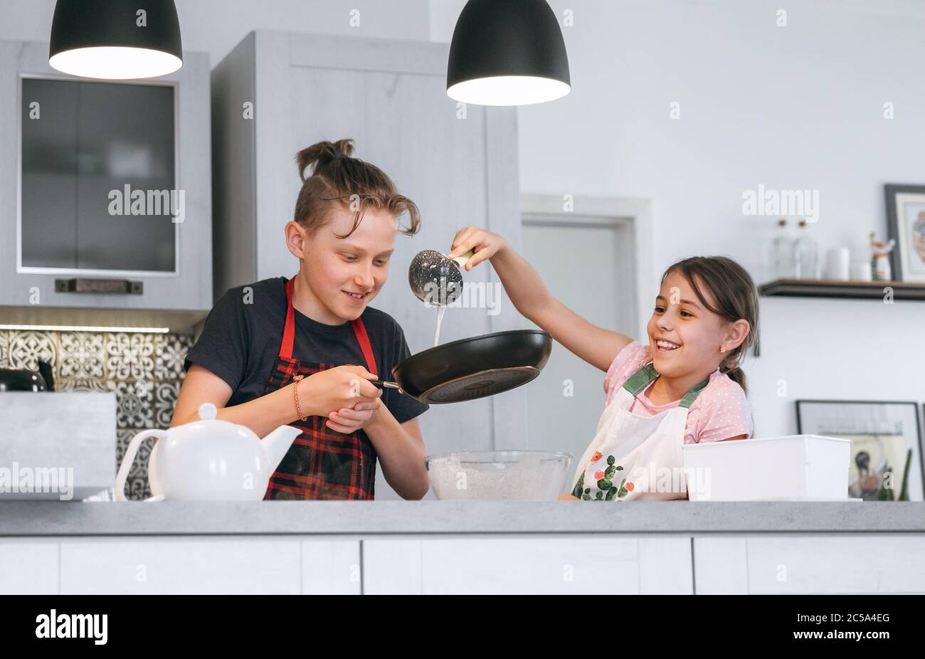 Image concept de cuisine maison pour enfants. Tabliers habillés par sœur et frère, faisant des crêpes maison dans la cuisine. Fille portant une pâte liquide sur le h Banque D'Images