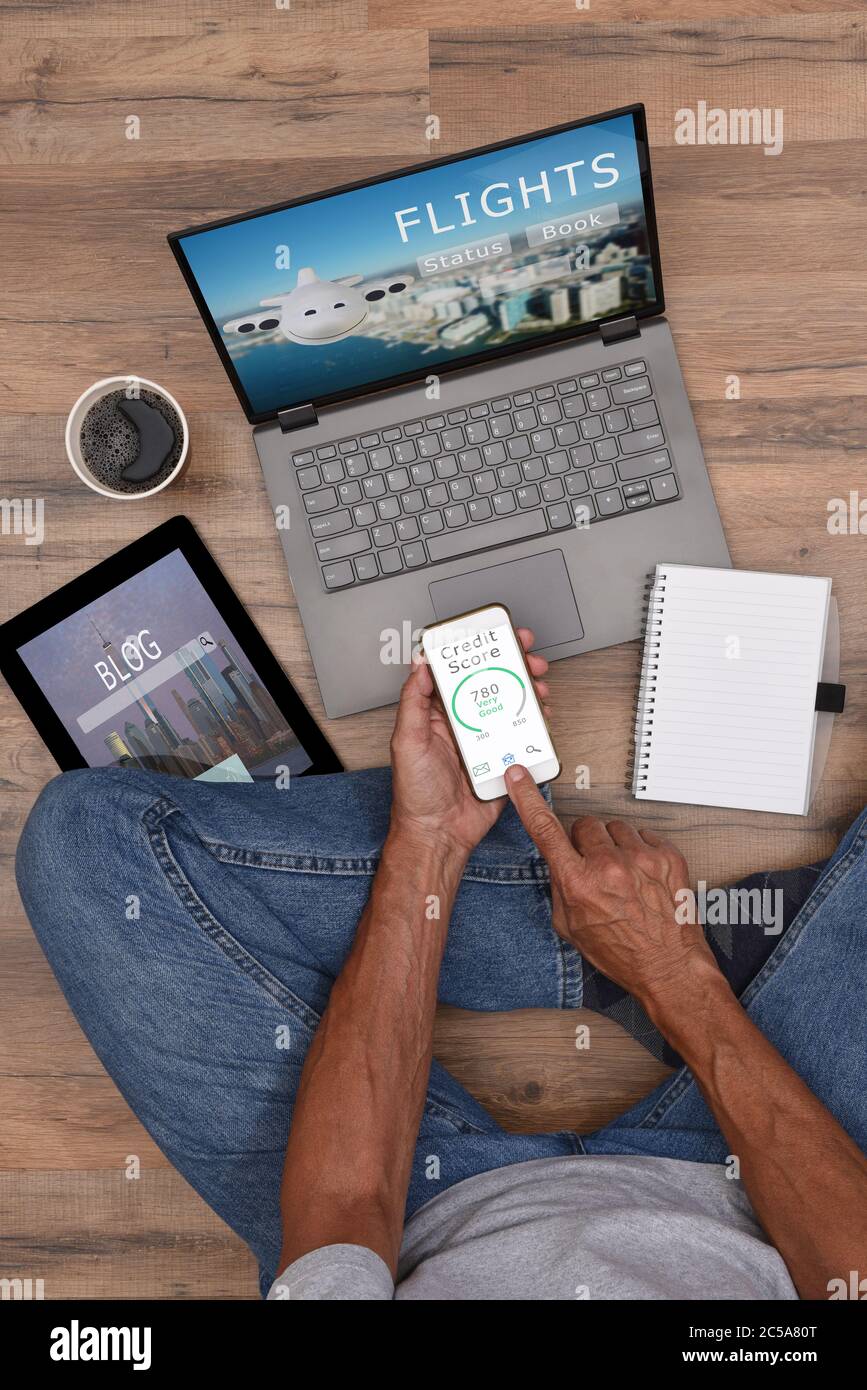 Angle élevé d'un homme assis sur le sol avec ses appareils électroniques - smartphone, ordinateur portable et tablette. Personne non reconnaissable vêtue de façon décontractée Banque D'Images