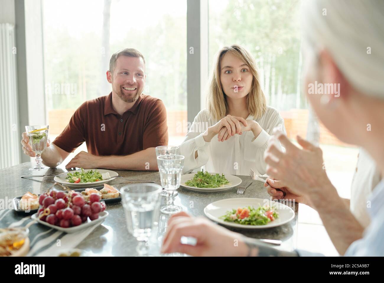 Jeune femme curieuse écoutant avec intérêt la mère pendant qu'elle discute pendant le dîner de famille Banque D'Images