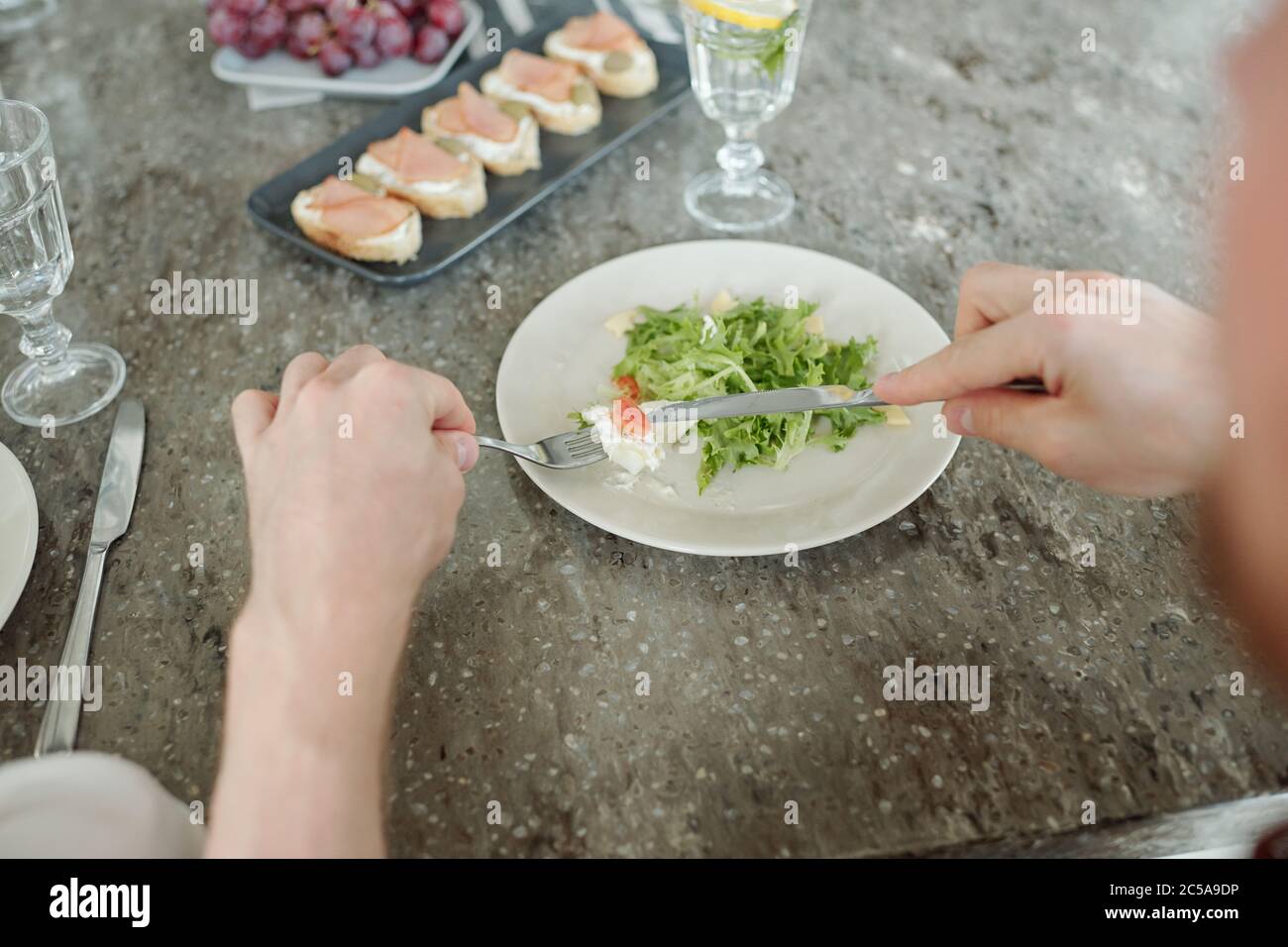 Gros plan d'un homme méconnaissable assis à table et mangeant une salade rafraîchissante à la fourchette et au couteau Banque D'Images