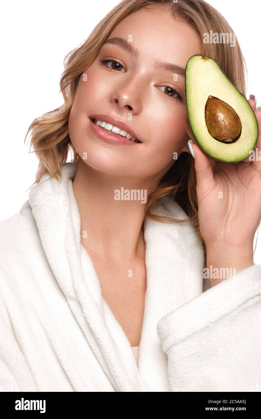 Belle jeune fille tendre dans un manteau blanc avec une peau propre et fraîche posant devant l'appareil photo avec avocat dans ses mains. Visage de beauté. Soins de la peau. Banque D'Images