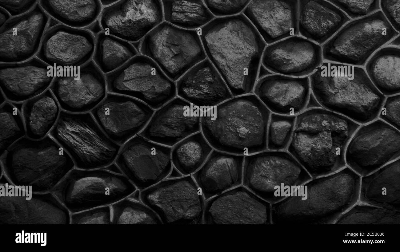 Mur monochrome gris foncé en pierre et ciment. Mosaïque de roches utilisées comme tuiles. Clôture en pierre noire et blanche. Texture décorative de matériau naturel Banque D'Images