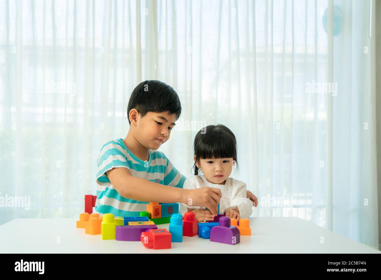 Un joli frère asiatique et sa sœur jouent avec un concepteur de blocs de jouets sur la table dans le salon à la maison. Concept de liaison de frère, d'amitié et d'apprentissage Banque D'Images