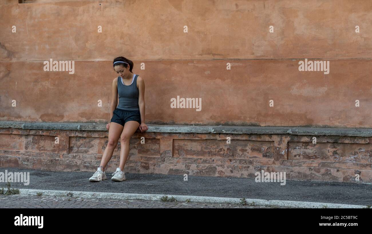 Jeune fille ado avec serre-tête, short, table de cuisson et baskets assis sur un banc de briques à Bolgona Italie Banque D'Images