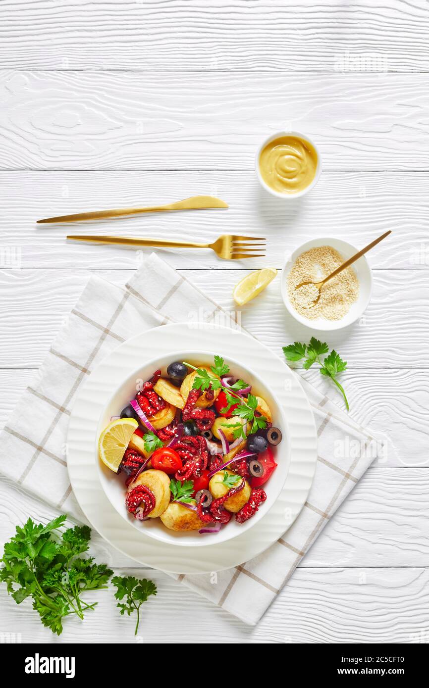 Salade de fruits de mer asiatiques de poulpes marinées avec jeunes pommes de terre, huile d'olive, citron, tomates, oignons, olives noires, graines de sésame avec couverts, sur un Banque D'Images