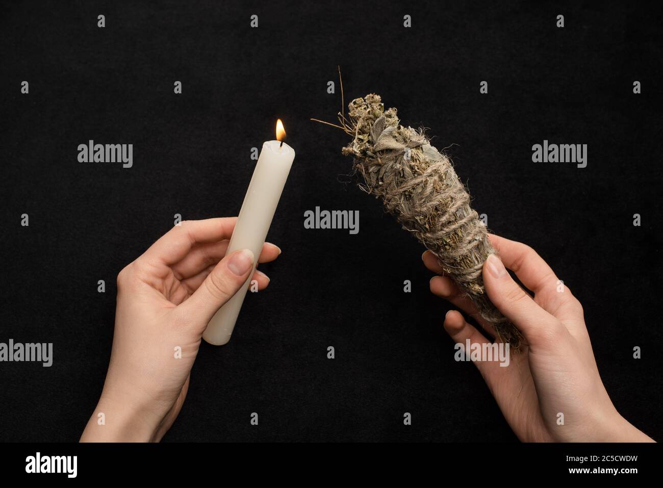 Vue courte du chaman tenant une bougie allumée et un bâton à taches isolé sur le noir Banque D'Images