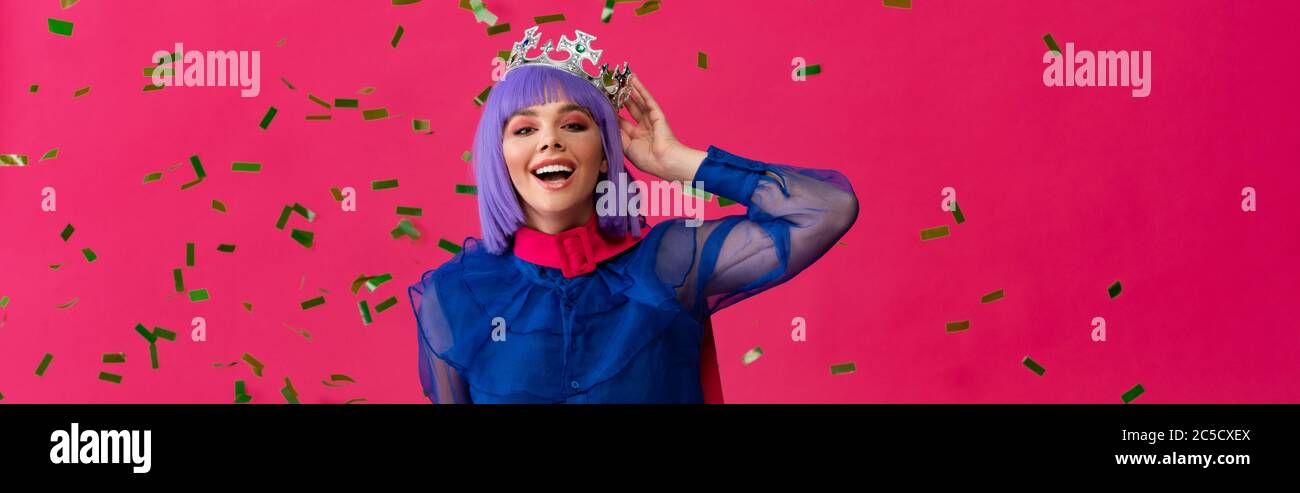 photo panoramique d'une jeune fille pop-art excitée dans une perruque pourpre et couronne sur la fête avec confetti, isolée sur rose Banque D'Images