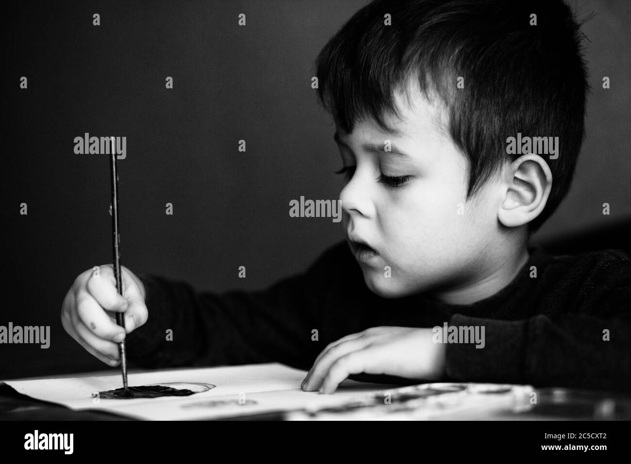 Un petit garçon dessine un pinceau et peint sa première photo Banque D'Images