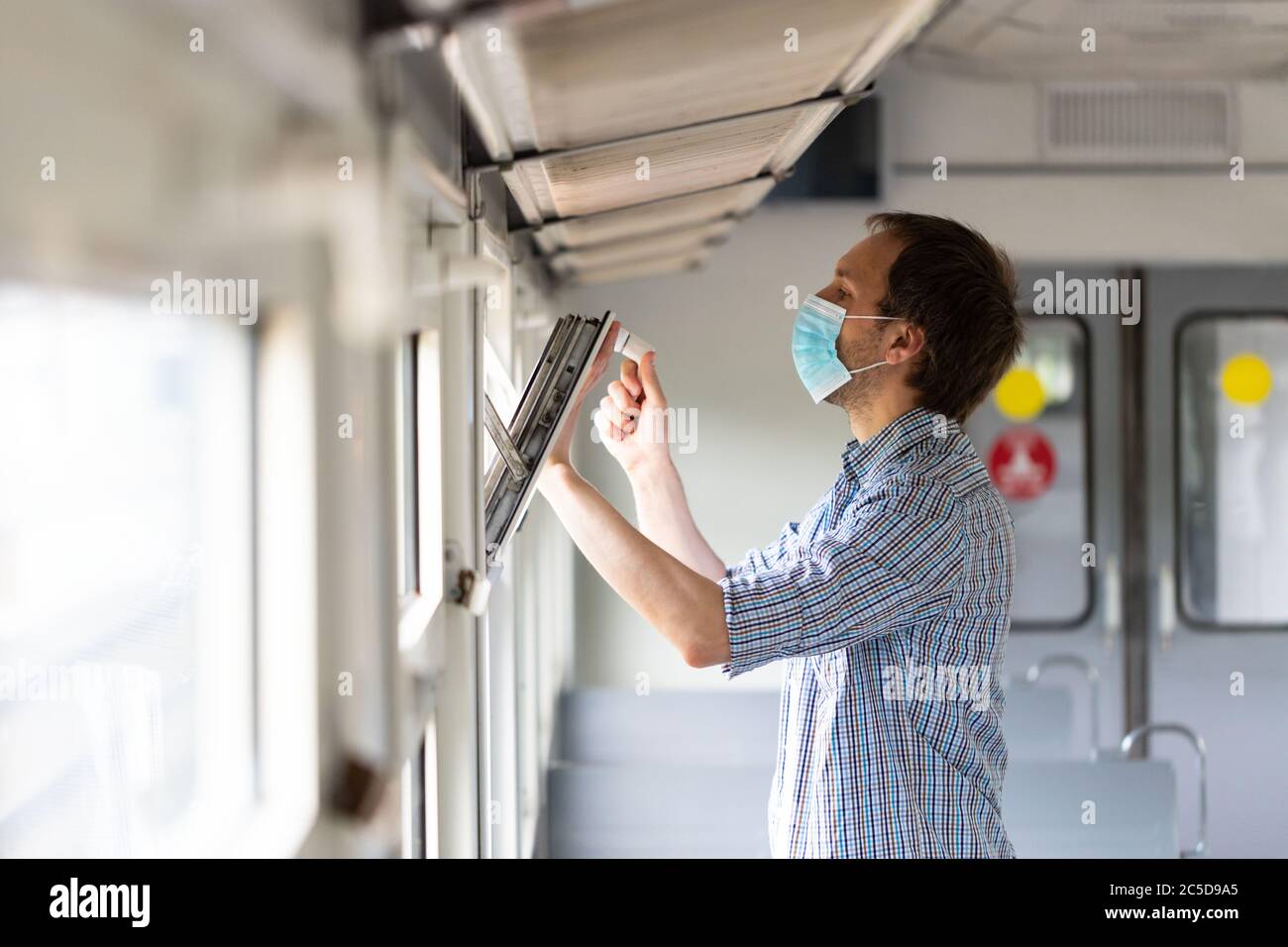 Homme dans une chemise à carreaux ouvre une fenêtre sur un train pour respirer l'air frais et la ventilation, portant un masque médical facial lors de nouveau changement normal après corona Banque D'Images