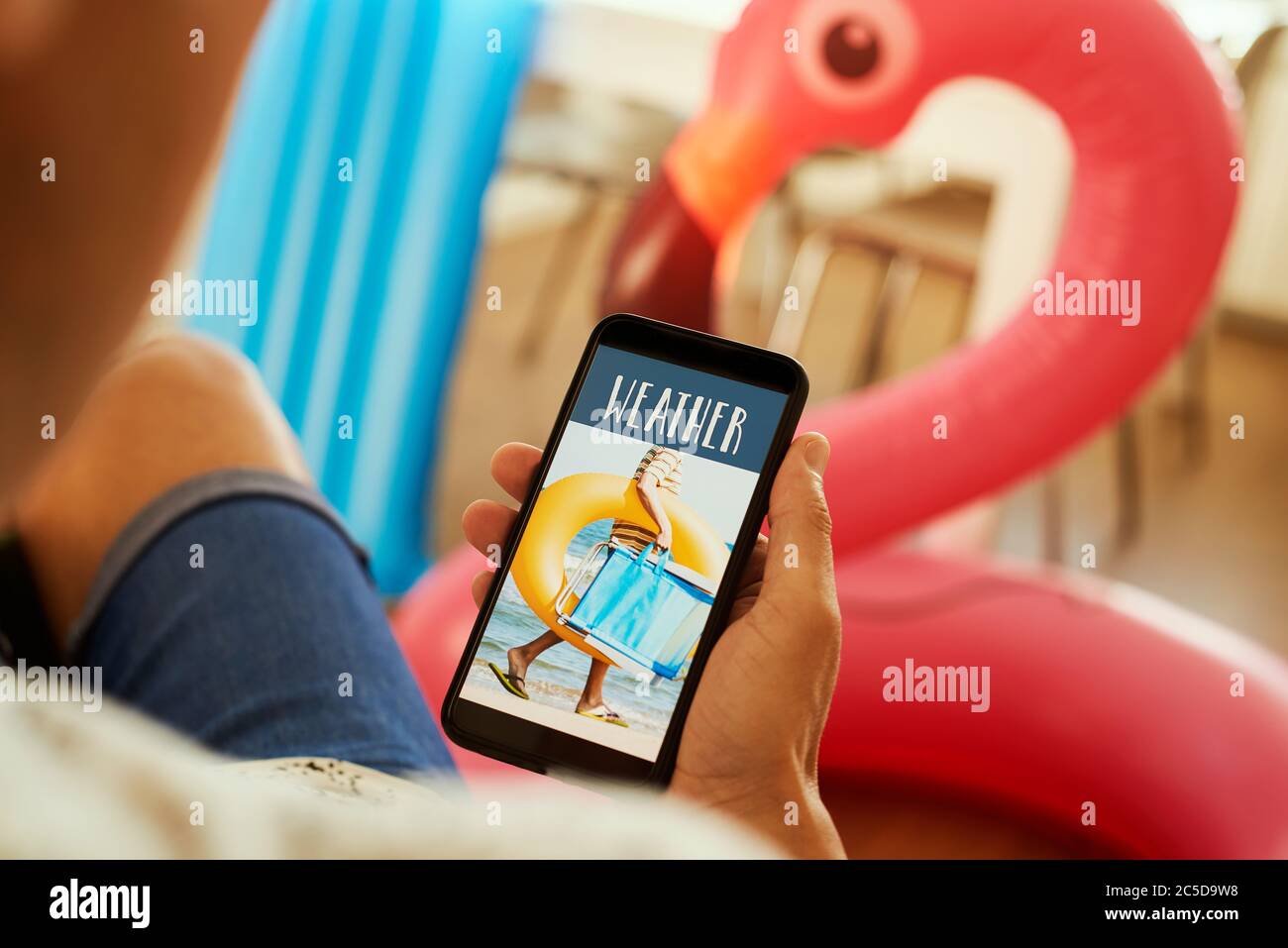 gros plan d'un jeune homme, portant des vêtements d'été décontractés, assis sur un fauteuil, ayant son smartphone dans les mains avec le texte météo dans son écran, Banque D'Images