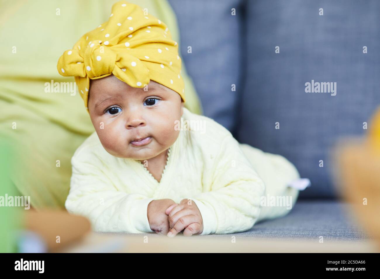 Portrait d'une petite fille mignonne avec un noeud sur la tête, allongé sur un canapé dans la chambre Banque D'Images