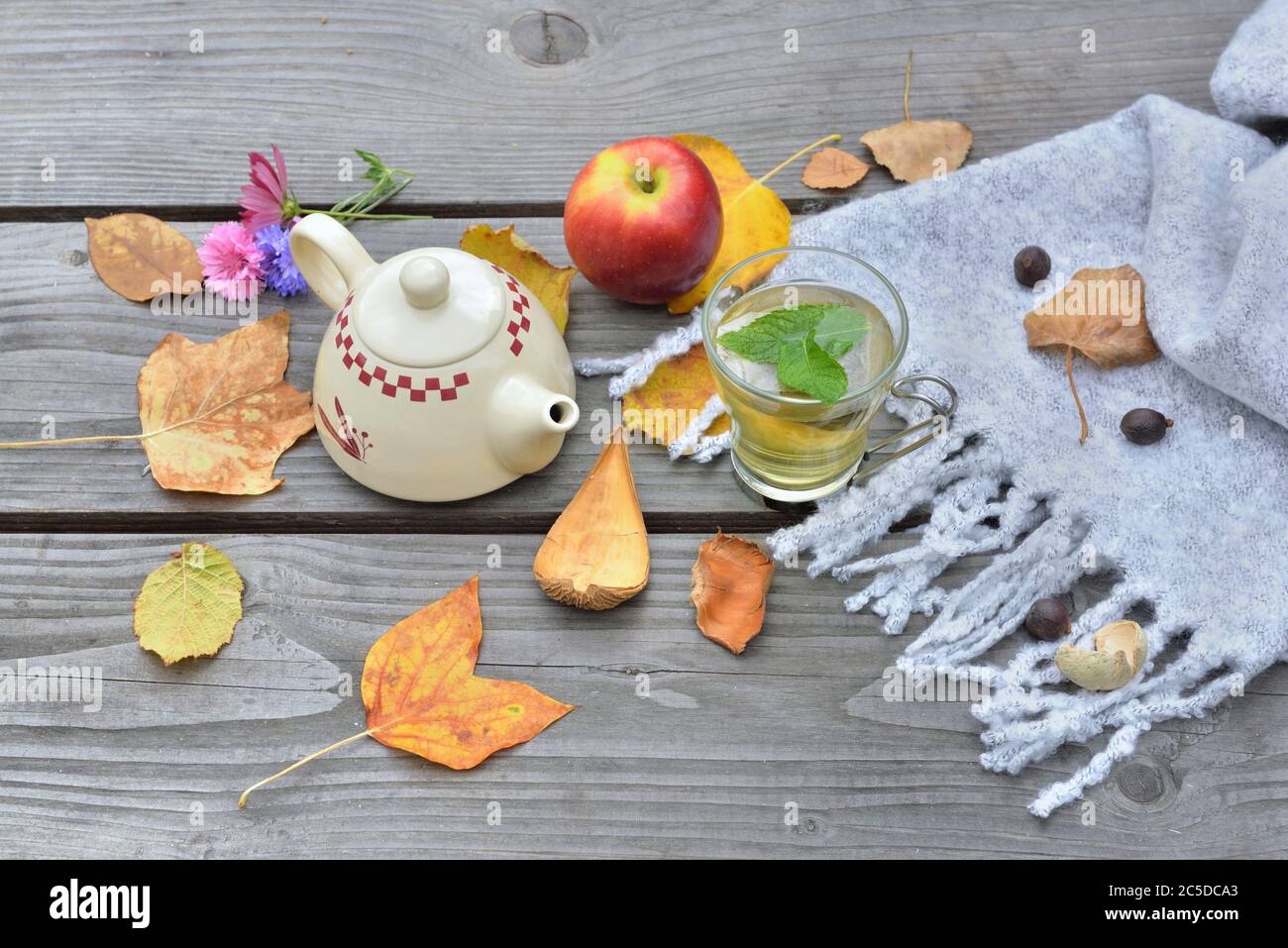 tasse de thé à la menthe sur une table en bois avec théière au milieu des feuilles automnales et pomme rouge sur foulard en laine Banque D'Images