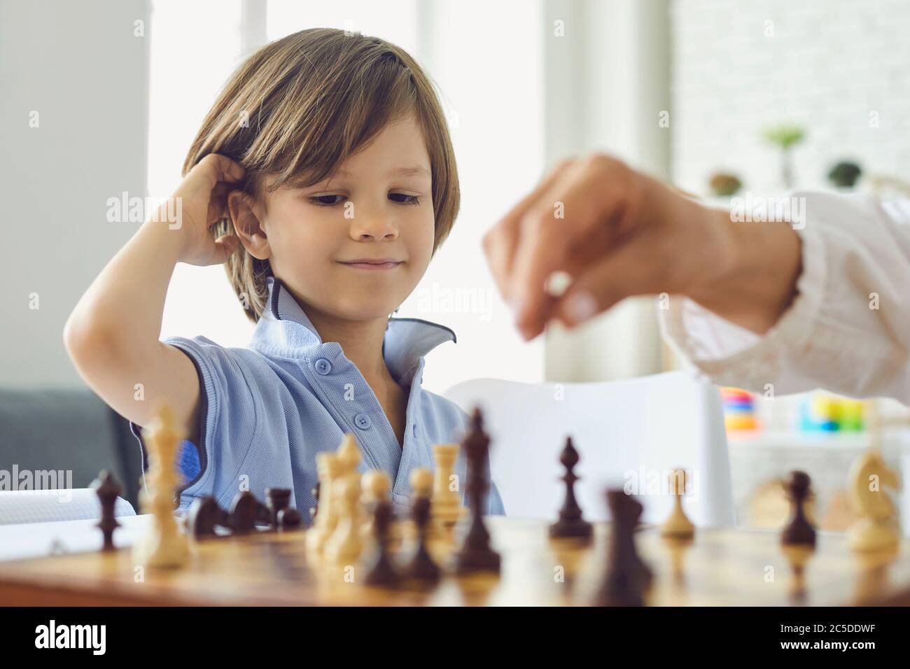 Adorable petit garçon jouant aux échecs avec sa mère à la maison. Enfant mignon appréciant jeu de stratégie de plateau avec ses parents à l'intérieur Banque D'Images