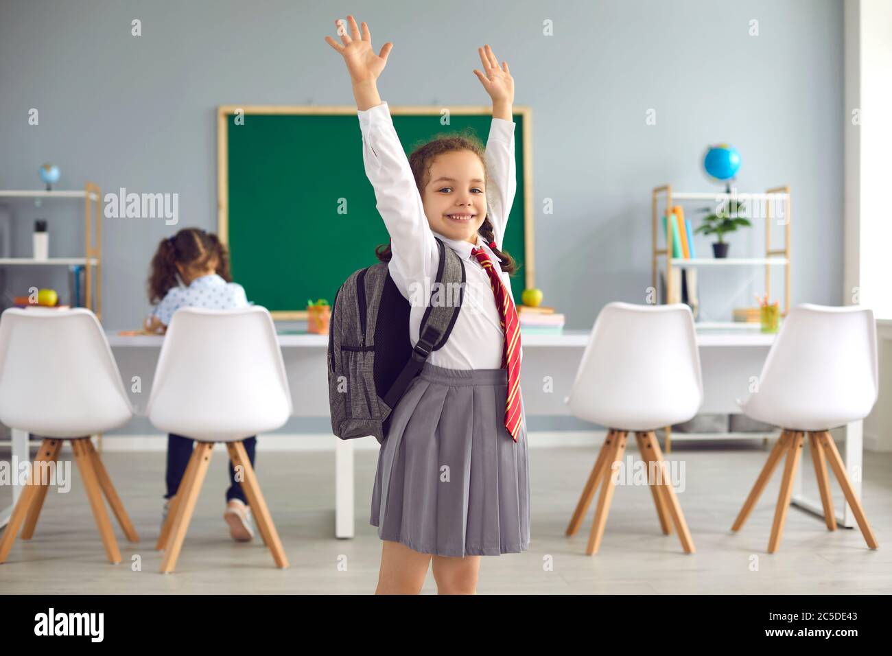 Concept de retour à l'école. Une écolière souriante lui a permis de lever les mains tout en étant debout en classe. Banque D'Images