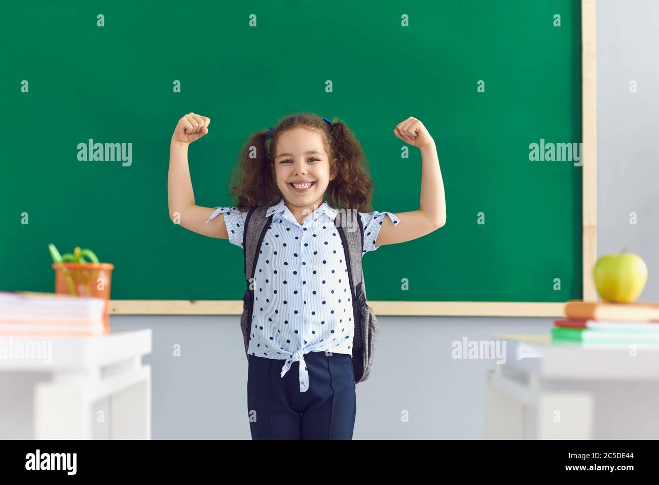 Douce fille montrant ses muscles en classe. Un enfant fort exprime sa motivation pour réussir. Retour à l'école Banque D'Images