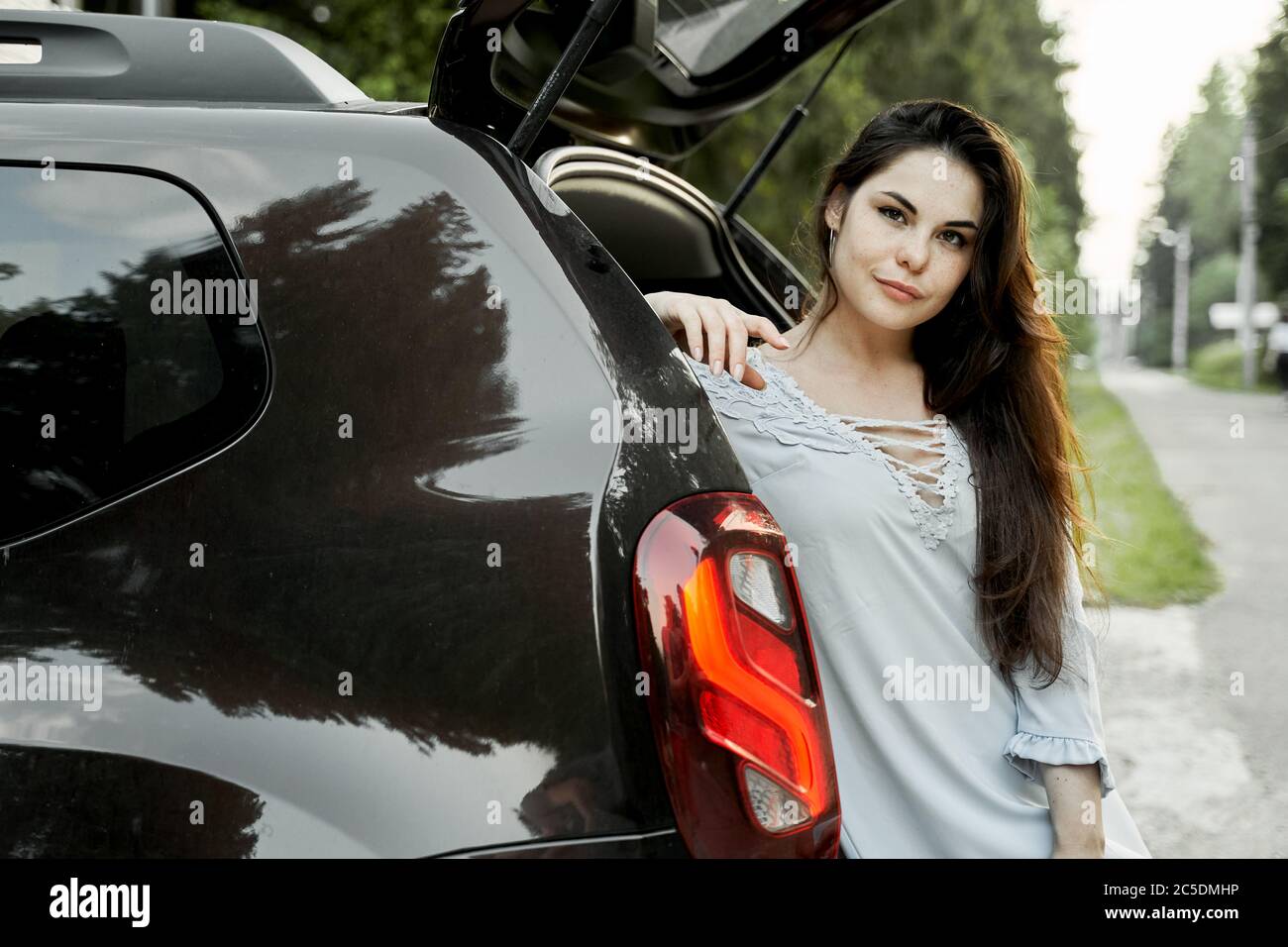 Jeune brunette debout près de la voiture noire le jour de l'été Banque D'Images