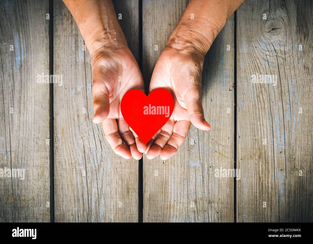 Femme âgée mains de près tenant coeur rouge. Arrière-plan rustique en bois. Amour, chaleur, prendre soin concept, Valentines, Fête des mères, donner, aide. Banque D'Images